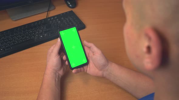 Top view of male hands holding mobile phone with green mock up screen