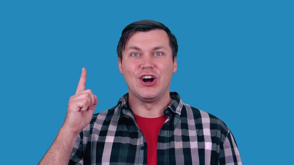 Portrait of happy man pointing fingers up at copy space, isolated on blue background. Idea.
