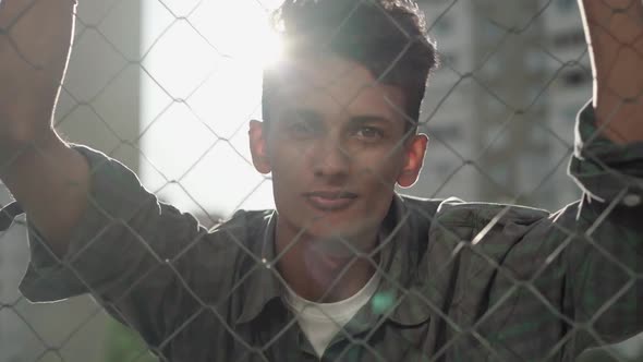 Close-up Portrait of Young African American Man in Sunlight Behind Mesh Fence. Happy Confident Guy alt