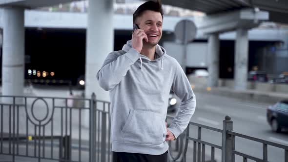 A young sports man receives a phone call outdoors near the road. alt