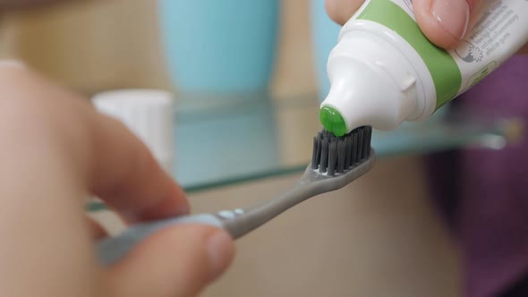 Women's Hands in the Bathroom Squeezes Green Toothpaste From a Tube Onto a Toothbrush Cleans Teeth