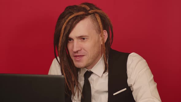 Young man works and conducts live broadcast on laptop on red background. alt