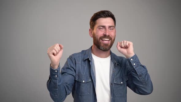 Photo of handsome young bearded man dancing isolated over grey wall background. alt