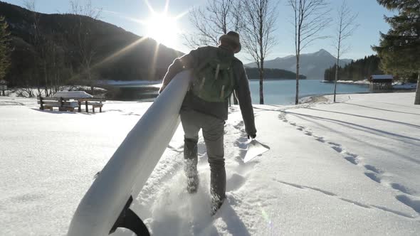Man carrying SUP through snow to a lake alt