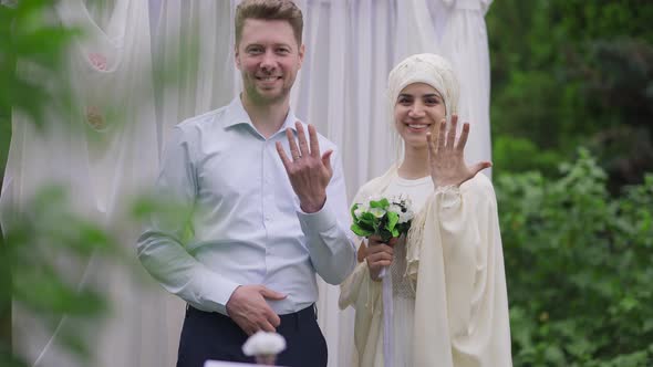 Loving Happy Middle Eastern Bride and Caucasian Groom Showing Wedding Rings Looking at Camera alt
