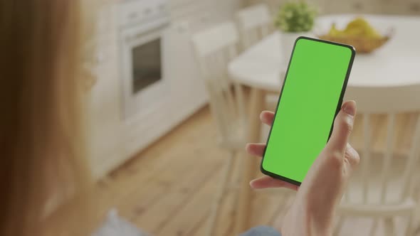 Handheld Camera Back View of Blond Woman Holding Chroma Key Green Screen Smartphone Watching Content alt