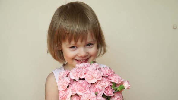 Little Girl Holds Bouquet of Pink Flowers Looks at Camera Laughs and Smells Flowers