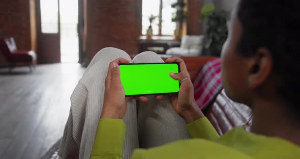 Young Woman Lying on Couch with Modern Smartphone in His Hand While Looking on Mock Up Screen alt