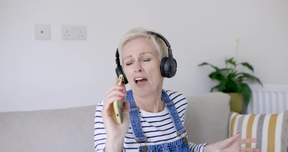 Woman sitting on couch singing and dancing to music from headphones