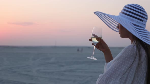 Elegant Woman with Glass of Wine Resting on Beach at Sunset