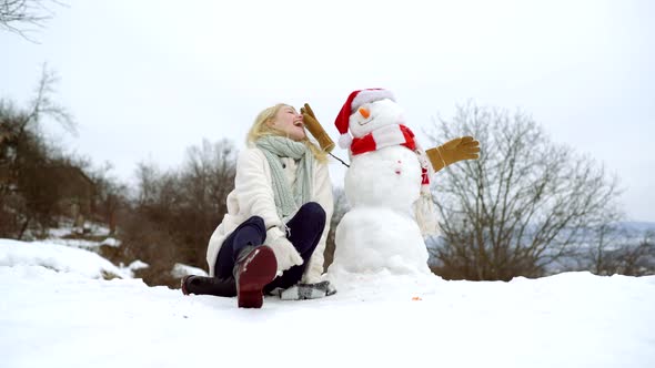 Winter Portrait of Young Beautiful Woman Make Snowman in Winter Garden. alt