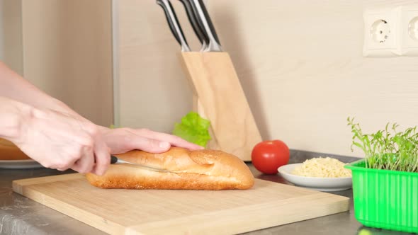 Women's hands cut bread for making sandwiches on a wooden cutting board.