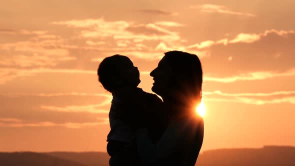 Young Happy Mom Gently Kisses Her Little Baby at Sunset