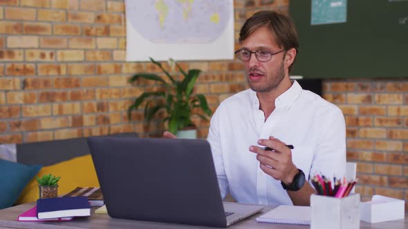 Caucasian male teacher teaching on videocall on laptop in the classroom at school alt