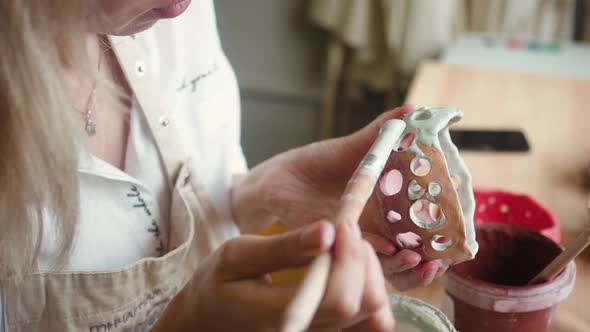 Close Up View of Female Potter Wearing Apron Using Glaze Brush to Paint on Pot alt