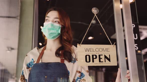 Business owner attractive young mixed race woman in apron hanging we're open sign alt