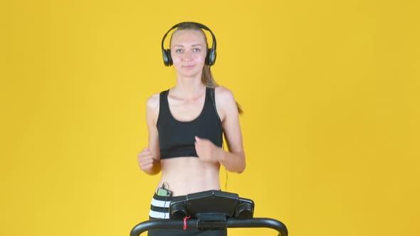 Fit blonde girl in sportswear with headphones trains on a treadmill.