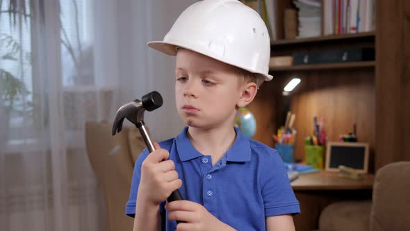 Portrait of a Little Boy in a White Helmet with a Hammer in His Hands at Home alt