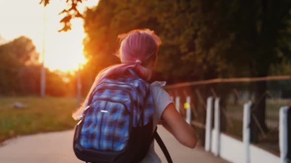 A Girl with a Schoolbag Behind Her Runs Along the Alley To the School in the Sun alt