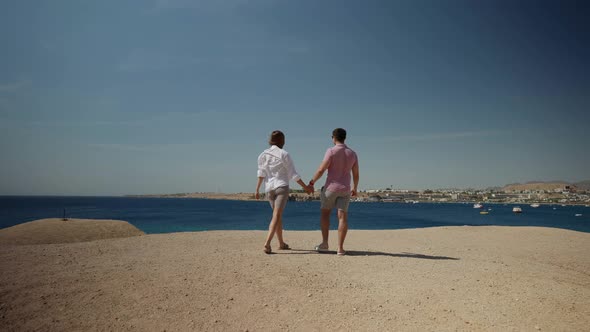 a Man in a Pink Tshirt and a Woman with Long Hair in a White Shirt Walk Away Along a Deserted Sandy alt