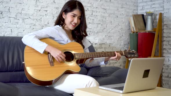 Young Asian Woman Learning How to Play Guitar on Laptop alt