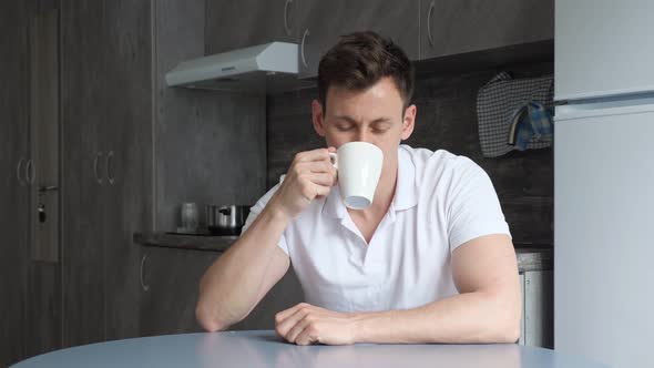 Sleepy Man Naps at Table and Drinks Cup of Coffee in Kitchen alt