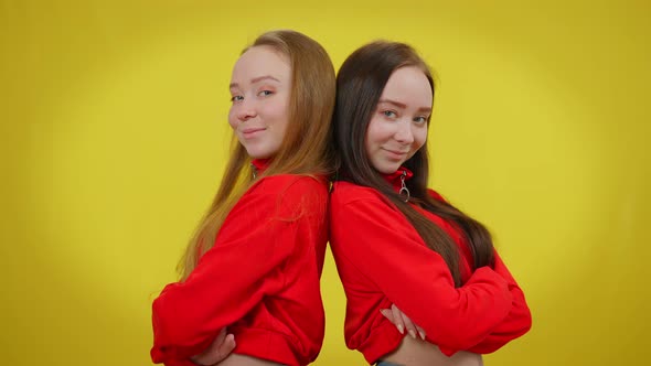 Two Slim Young Women Posing Back to Back Smiling Standing at Yellow Background alt