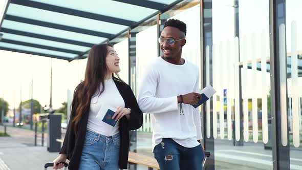 African American and His Asian Female Friend Walking on Bus Station with Suitcases alt