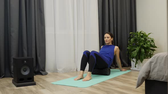 Beautiful female massages buttock muscles using fascia roll on yoga mat alt