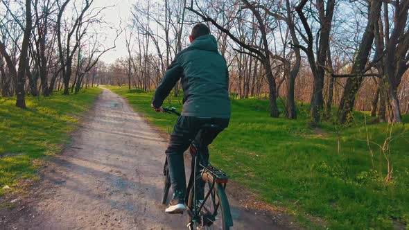 Young Guy Rides a Bicycle Along a Path in a Green Forest Rear View in Slow Mo alt