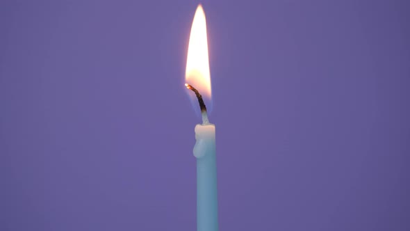 One Blue Cake Candle Burning on a Purple Background