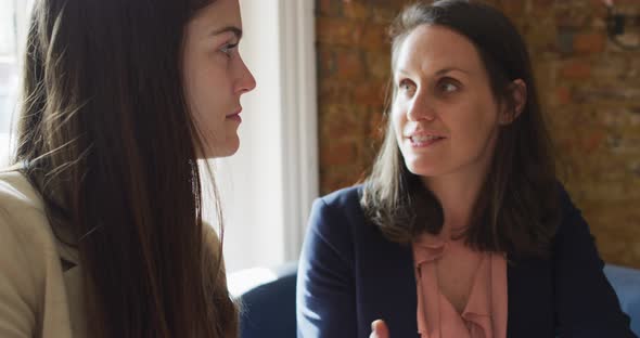 Portrait of two caucasian businesswomen sitting at table, talking, having business meeting alt