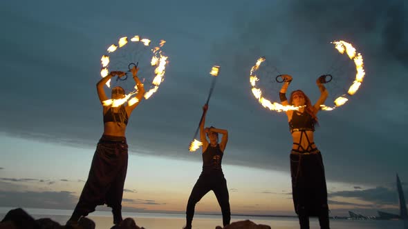 A Beautiful Young Team Makes a Fire Show Against the Backdrop of the Sunset Sky and the River