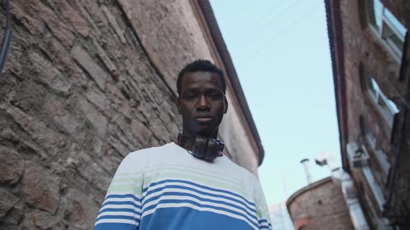 A Young Black Student with Headphones Walks Through the City Centre at Sunset