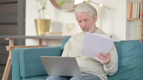 Old Man with Documents Working on Laptop on Sofa alt