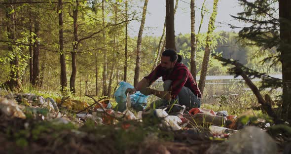 A Male Volunteer Collects Trash Scattered in the Forest in a Plastic Bag