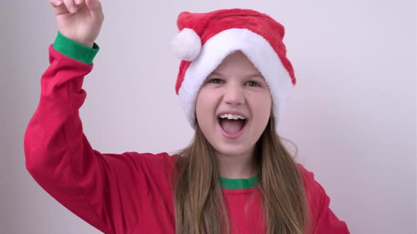 Little Cute Girl in Christmas Red Hat Showing Thumbs Up and Pointing Empty Place Advertising Area alt