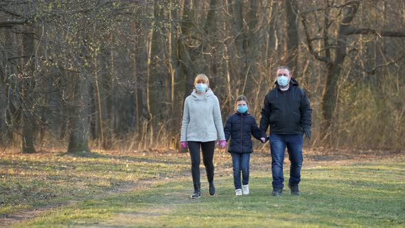 Mom, Dad and Daughter Walk in the Spring Park in Medical Masks . The Concept of Protection Against