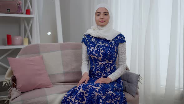 Live Camera Zoom in to Shy Slim Beautiful Muslim Woman in Blue Wedding Dress Sitting on Couch alt