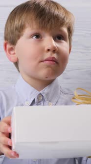 The Boy Was Given a Box with a Gift He Looks at It on a Wooden Background alt
