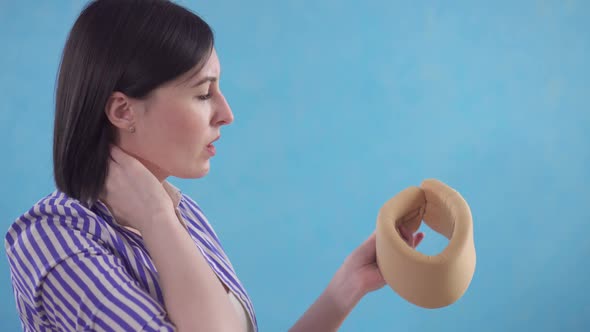 Young Woman Puts on a Protective Collar Against Neck Pain Standing on a Blue Background alt