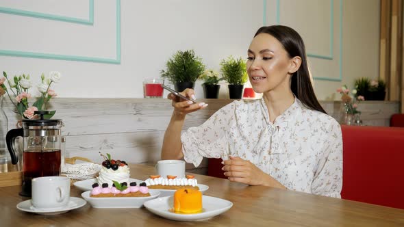 Smiling Girl Takes Picture of Cakes and Tea at Table in Cafe alt