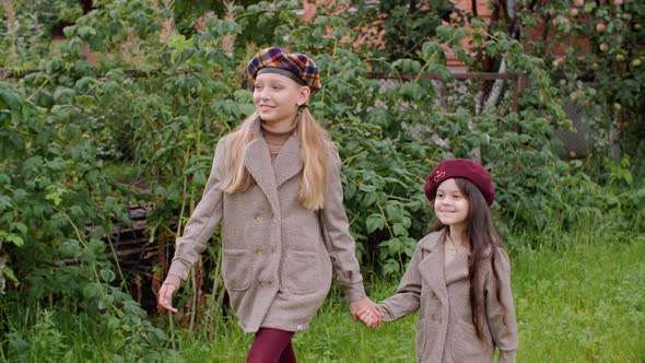 Cute Smiling Girls in Berets Holding Hands and Walking in Garden alt