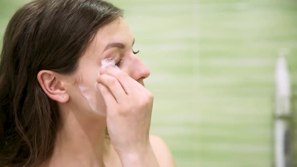 Girl Removes Makeup Using a Cotton Pad in a Green Bathroom alt