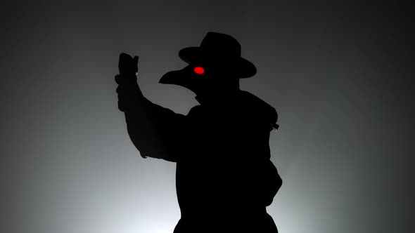 Plague Doctor with Crow-like Mask Puts on Gloves Isolated on Black Smoke Background. Creepy Mask alt