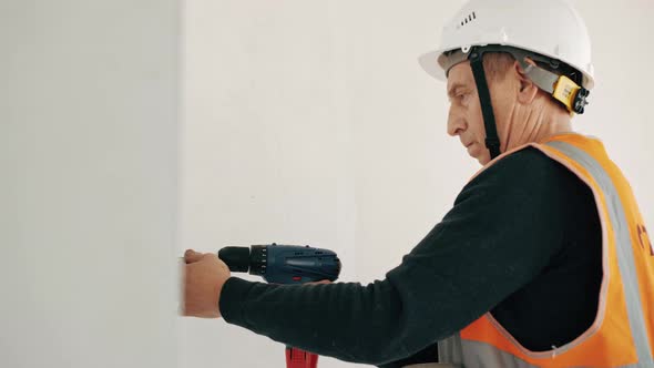 Mature foreman using electric screwdriver. Renovation concept. Screwing screws into wall. Building n alt