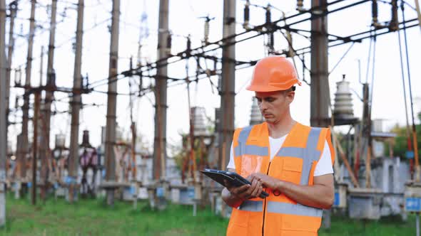 Portrait of Male Engineer in Uniform and Helmet Standing Outdoor and Tapping on Tablet