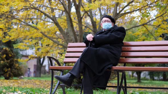 An Old Sad Grandfather is Sitting on a Bench in a Park in New York alt