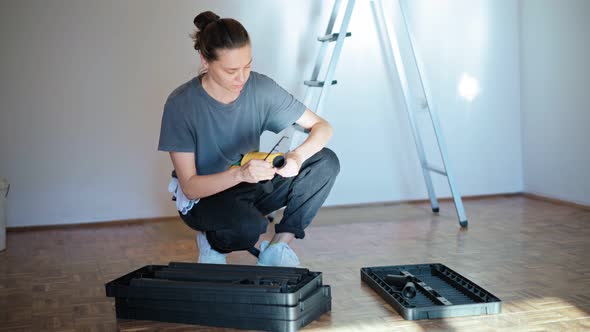 Professional Repairwoman with Tool Belt Assembles a Plastic Shelf From Parts alt