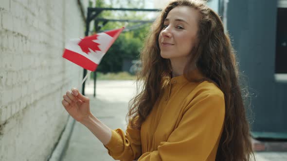 Portrait of Happy Young Lady Waving Canadian Flag Smiling Standing Outdoors in City alt